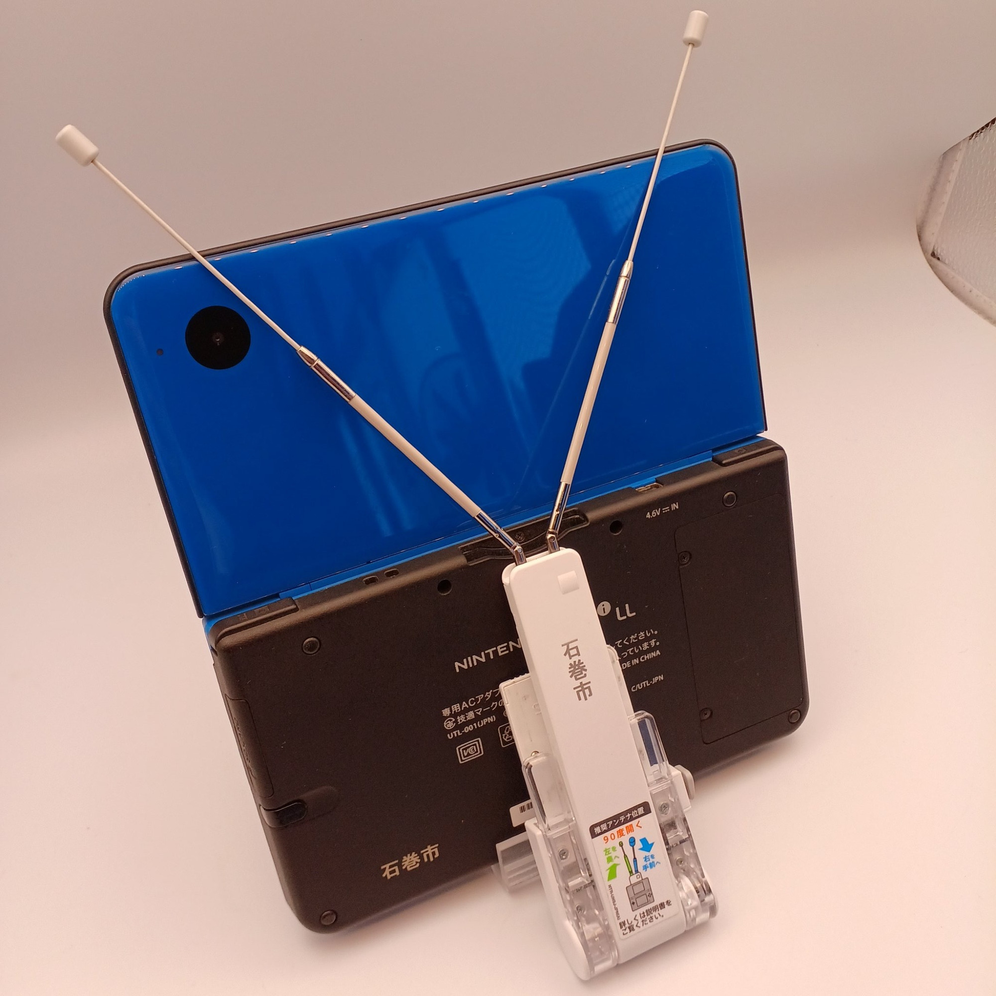 Back side photo of a blue Nintendo DSi LL with a digital TV tuner (DSテレビ). There’s a “Ishinomaki City” engraving on the back of the console and also the tuner.
