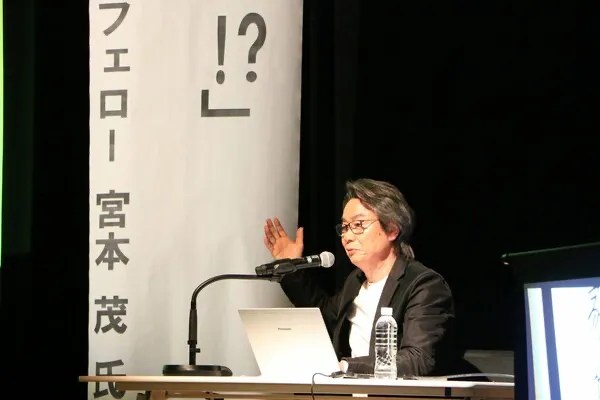 Shigeru Miyamoto gave a speech on stage next to a banner, with a mic and laptop in front of him; source: Nantan City via Kyoto Shimbun