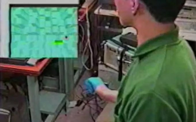 A composite image of: 1. Screenshot of a 3D game (content unclear) being developed by Casio then 2. Photo of a man wearing a blue glove on one hand, presumably controlling the game