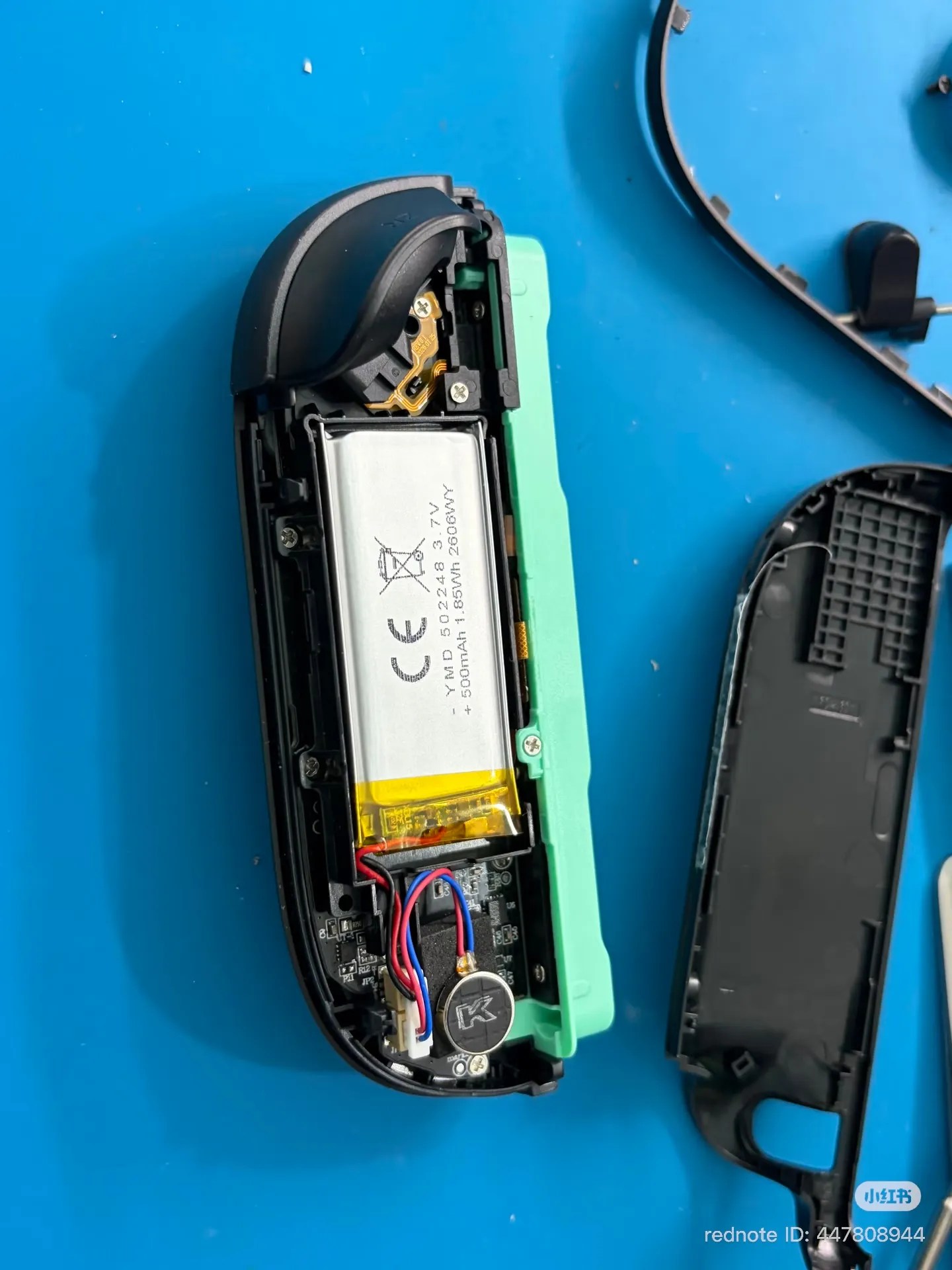 Photo of a counterfeit Joy-Con 2 (right, green), back side interior with the back shell removed, showing the battery and a rotary motor