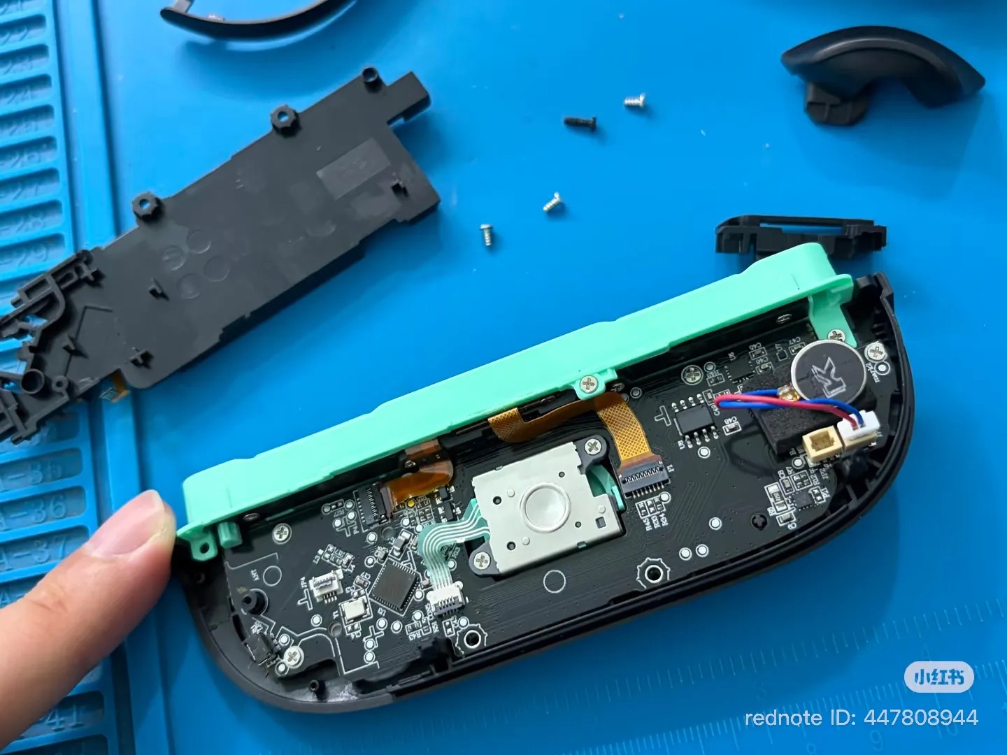 Photo of a counterfeit Joy-Con 2 (right, green), back side interior with the battery compartment removed, showing the circuitry, bottom of analog stick, and a rotary motor